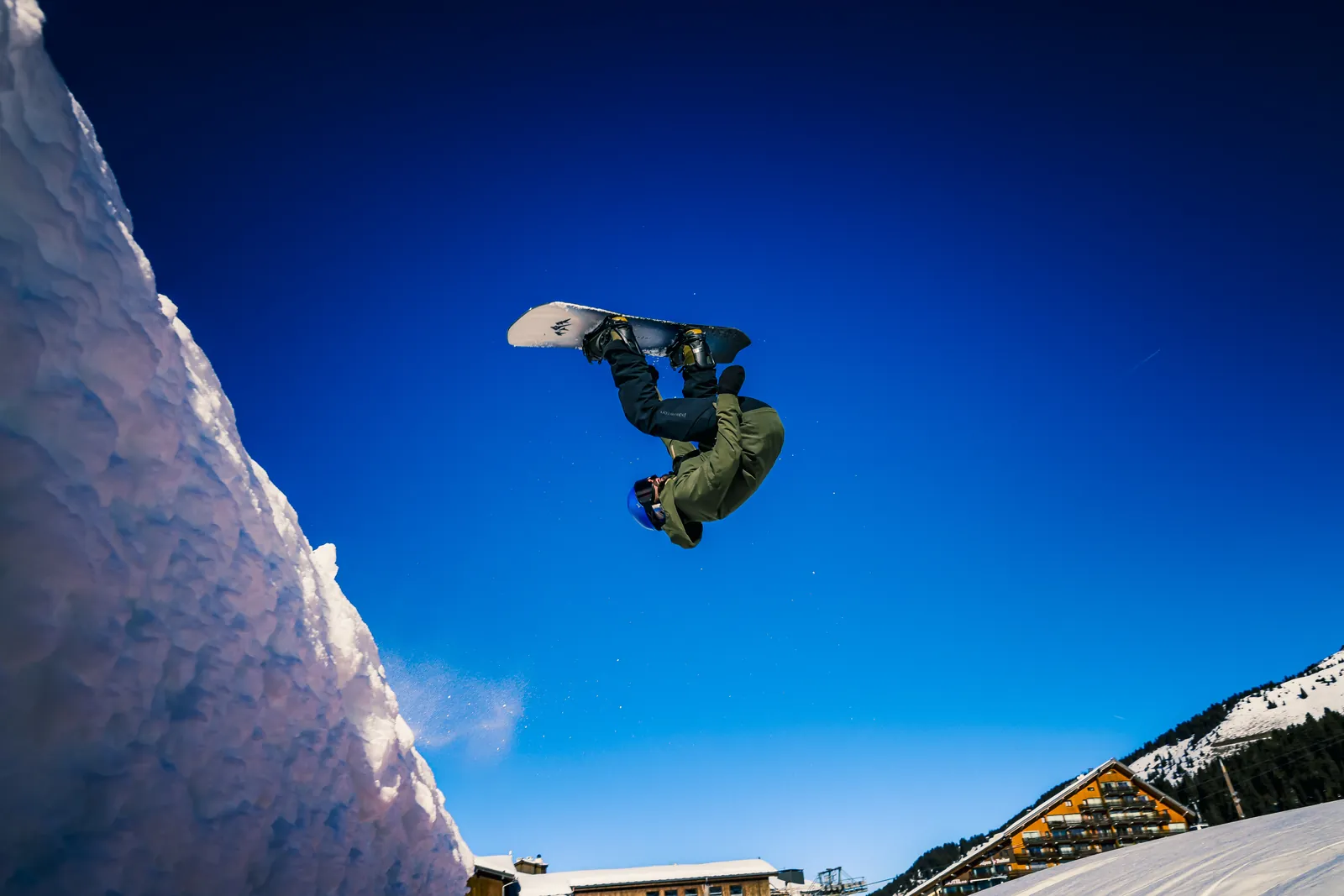 Nathan Delacoste en plein saut en snowboard, sous un ciel bleu